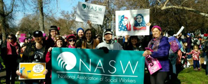 people standing at a rally hold posters, some with NASW logo