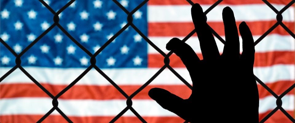 hand against chainlink fence with american flag in background